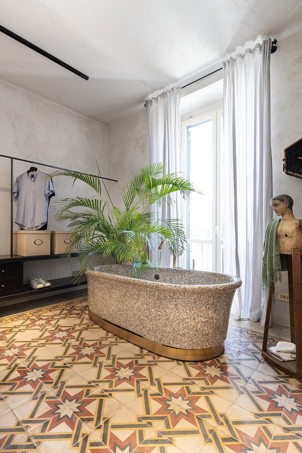 Bright, airy room with a unique terrazzo floor pattern and a rustic bathtub surrounded by lush greenery.