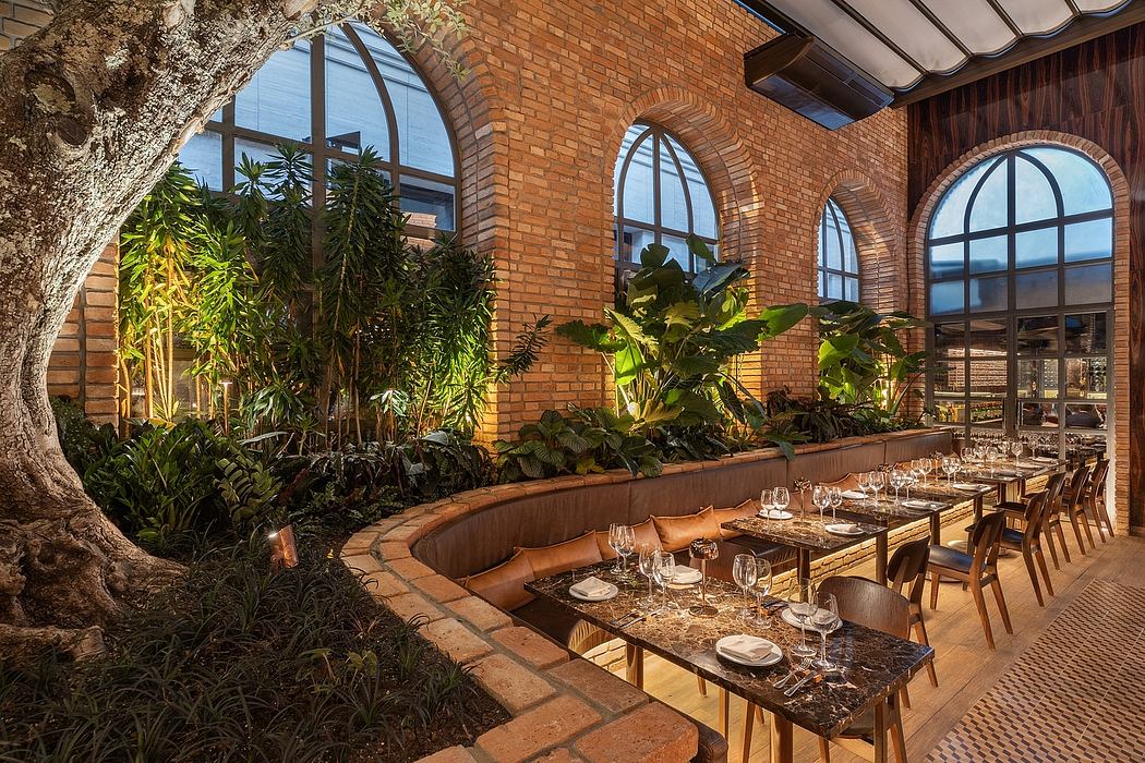 A cozy brick-walled restaurant with lush tropical plants and arched windows, a rustic yet elegant setting.