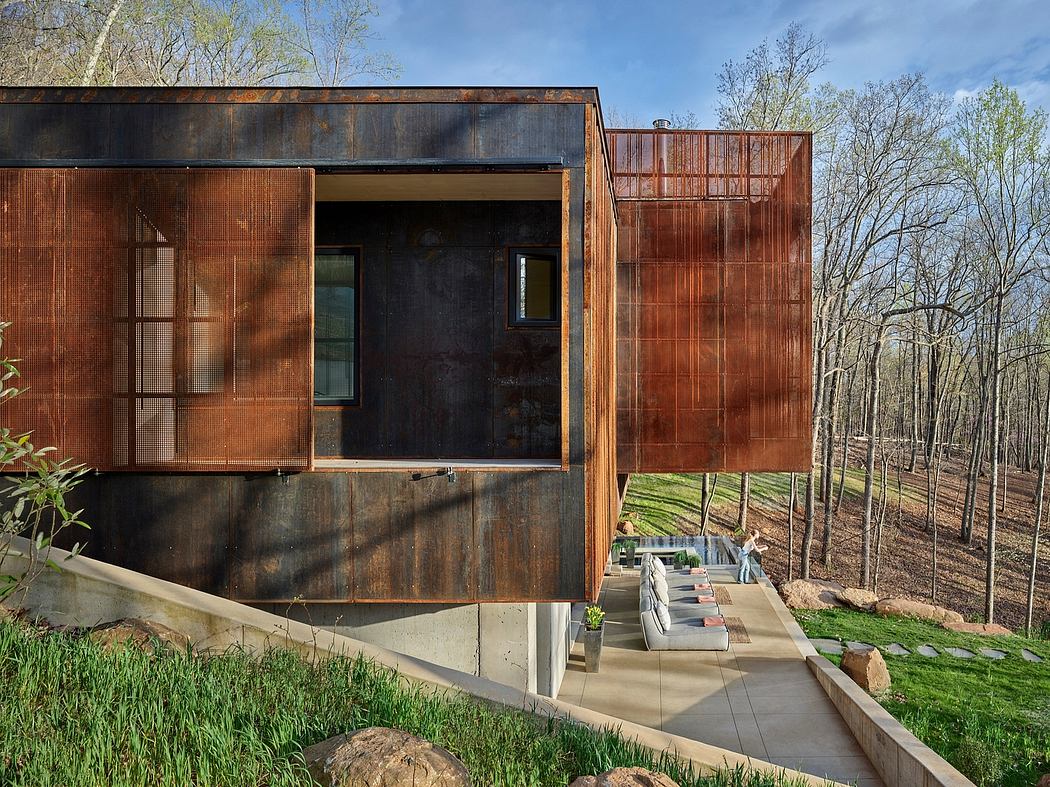 Rustic modern cabin with concrete patio, wooden siding, and lush forest surroundings.