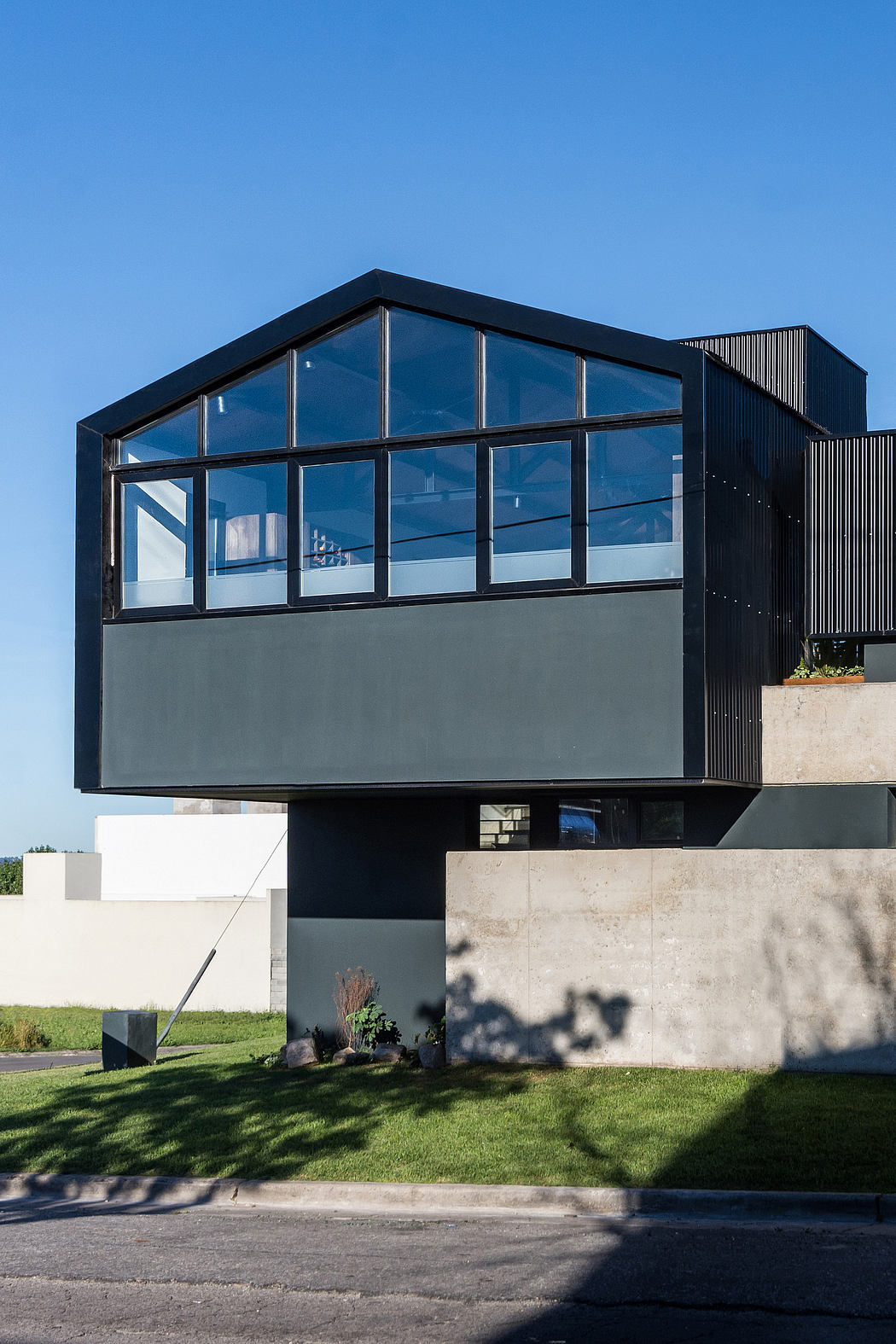 A modern, glass-enclosed structure with a black exterior and a concrete base, set against a grassy landscape.