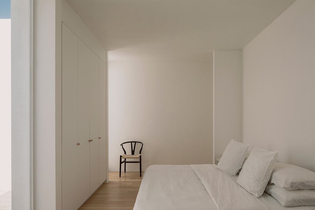 A minimalist bedroom with clean lines, light walls, and a simple wooden chair.
