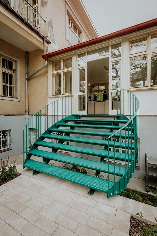 Ornate building exterior with bold green metal staircase and large glass windows.