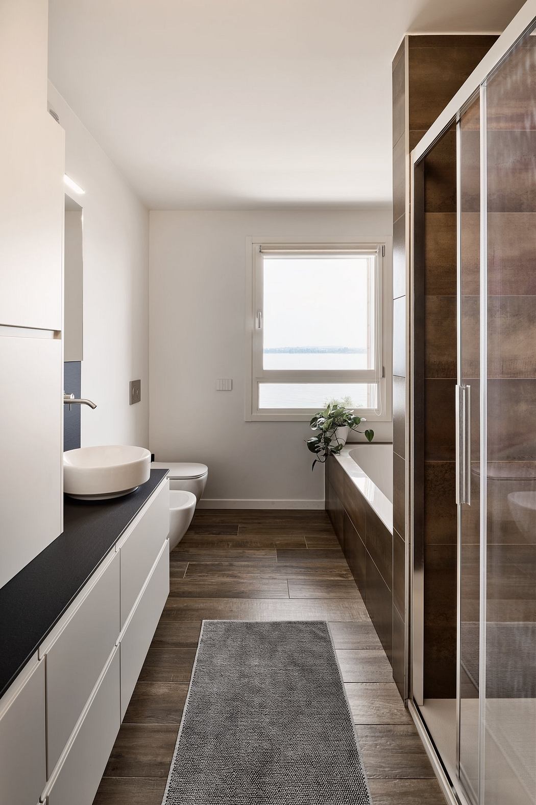 A minimalist bathroom with wooden floor tiles, a vessel sink, and a window overlooking the outdoors.