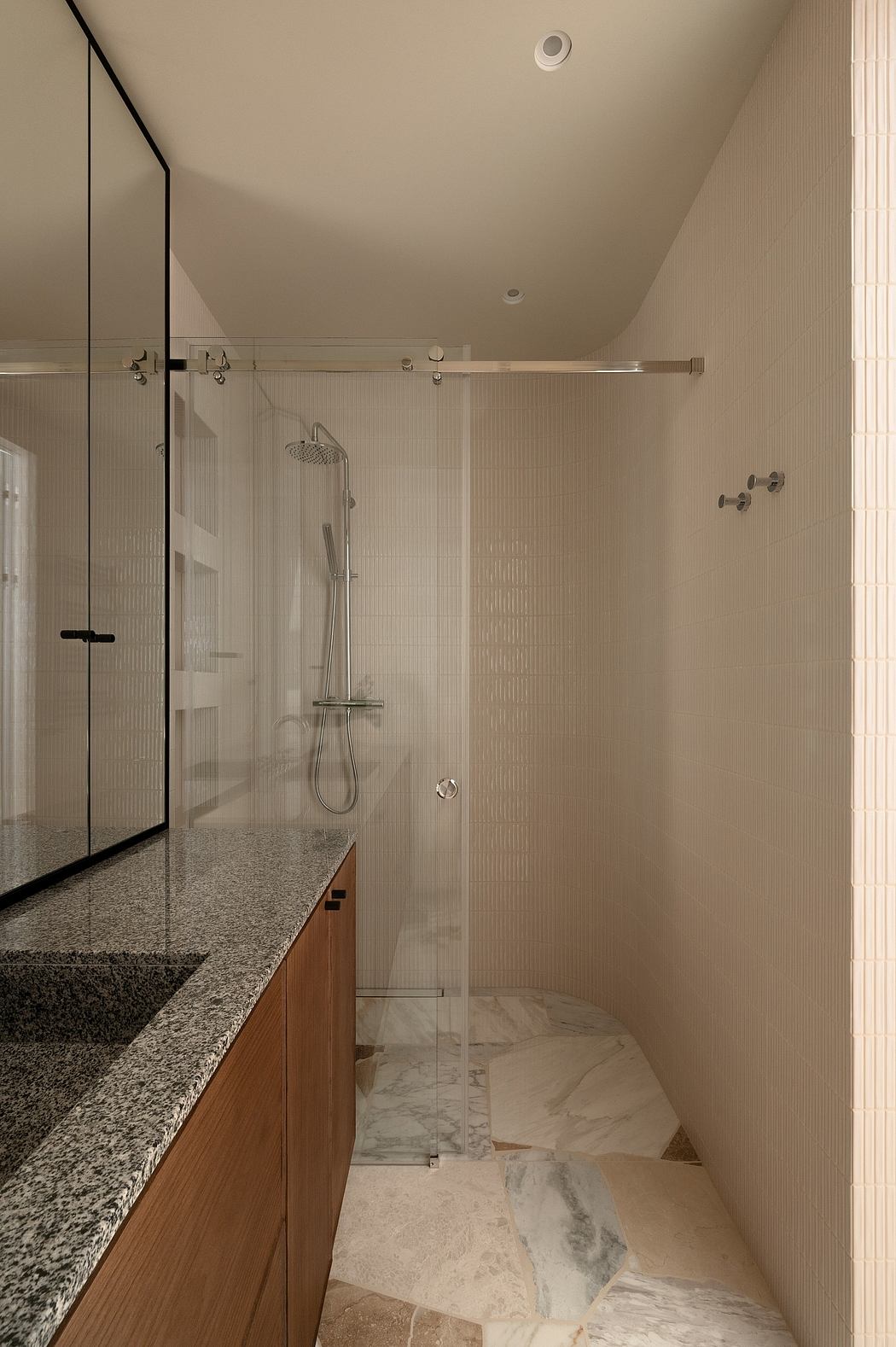 A modern bathroom with a glass shower enclosure, granite vanity, and marble flooring.