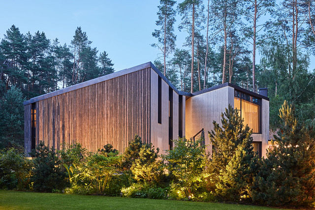A modern, wooden-slatted building with large windows, set in a lush forest landscape.
