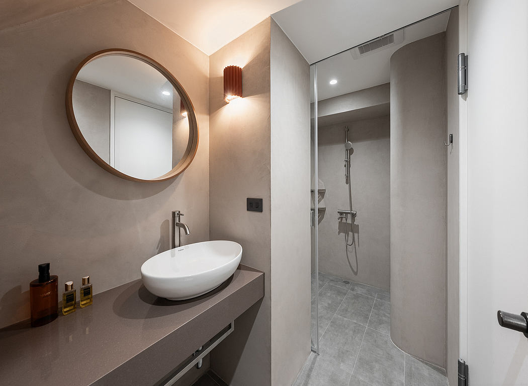 Sleek, modern bathroom with round mirror, vessel sink, and glass-enclosed shower.