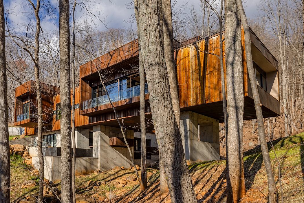 A modern, wooden cabin-style structure nestled among bare trees, with large windows and cantilevered balconies.