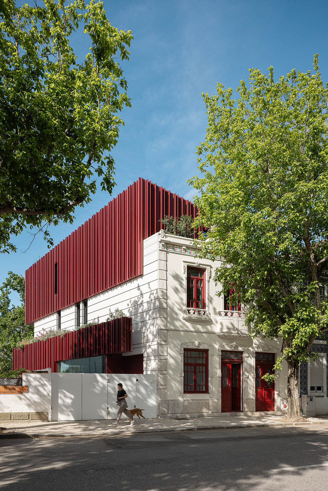 A modern red-panelled building with ornate windows and doorways, surrounded by lush greenery.