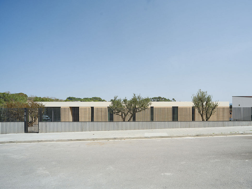 Minimalist modern facade with vertical slats, surrounded by trees and a paved area.