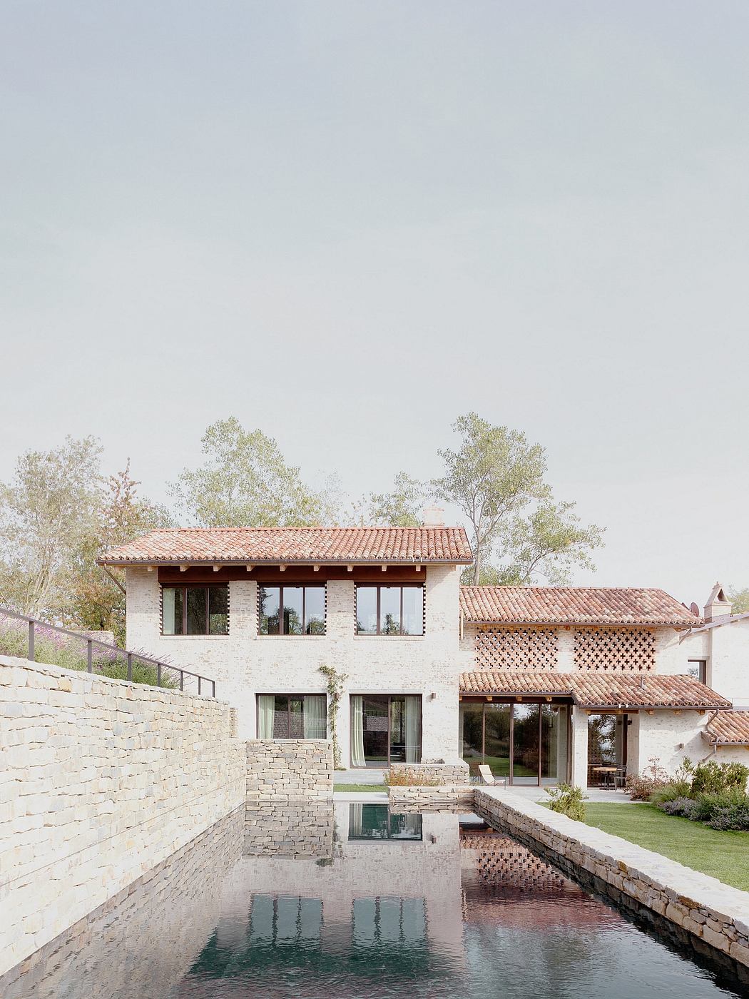 A modern villa with a tiled roof, stonework, and a reflection pool in the foreground.