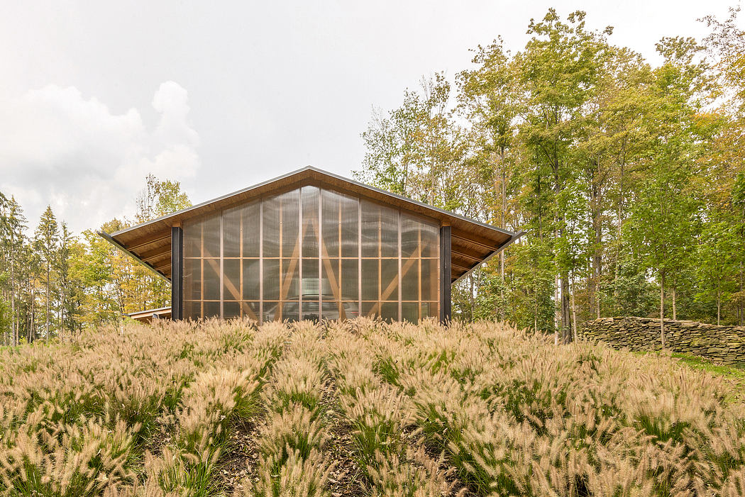 A modern wooden-framed structure with expansive glass walls, surrounded by lush foliage.