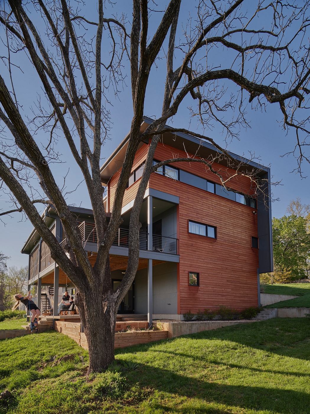 Modern, multi-level wood-clad house with clean lines, large windows, and a lush green lawn.