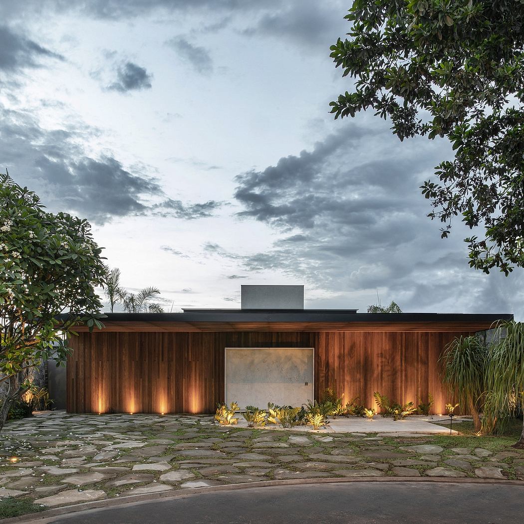 Striking modern home with wooden facade and illuminated landscaping under cloudy sky.