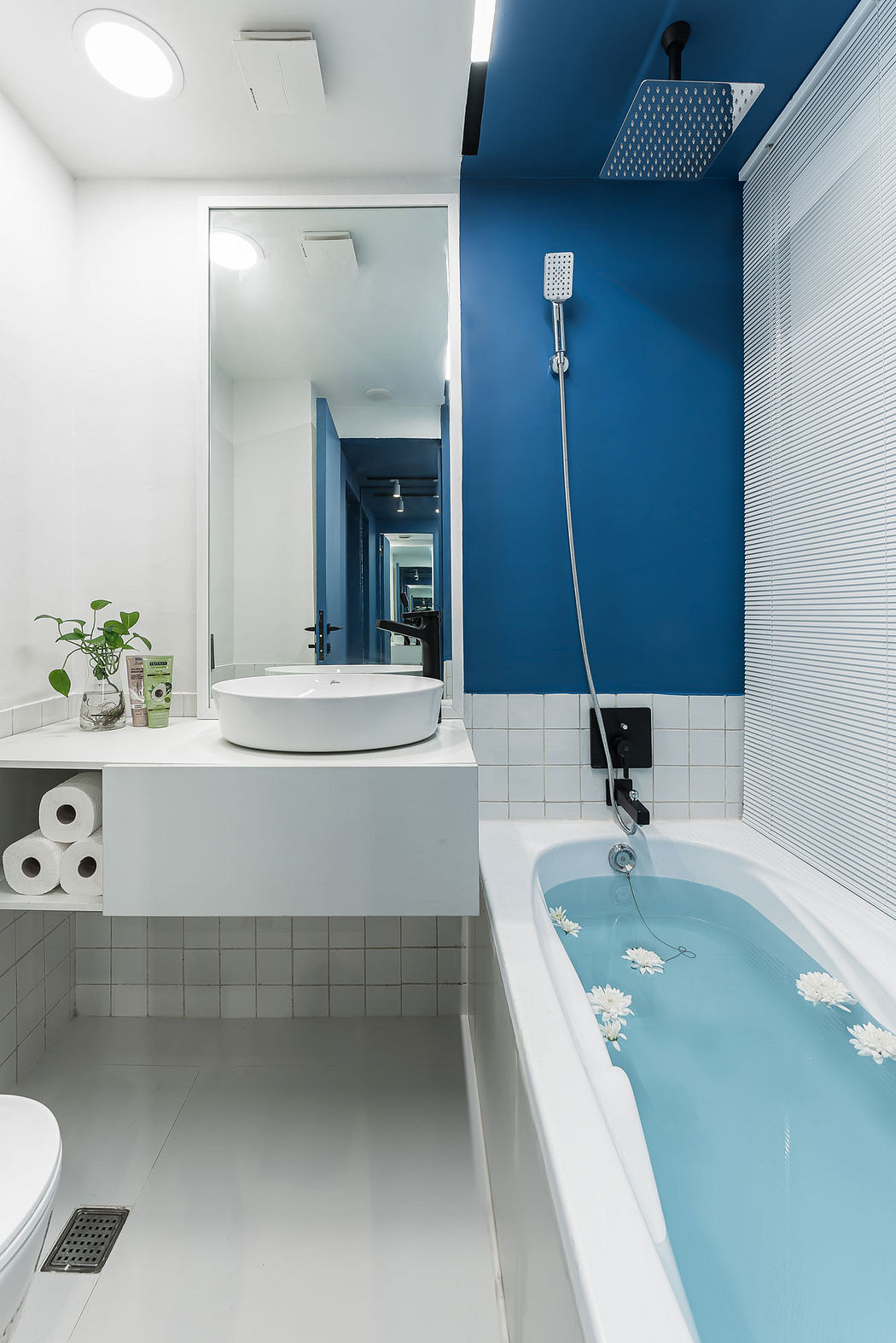 A modern bathroom with a white vanity, blue tiled walls, and a patterned bathtub.