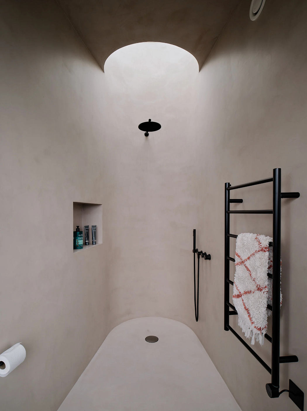 Minimalist bathroom with curved walls, circular skylight, and modern black fixtures.