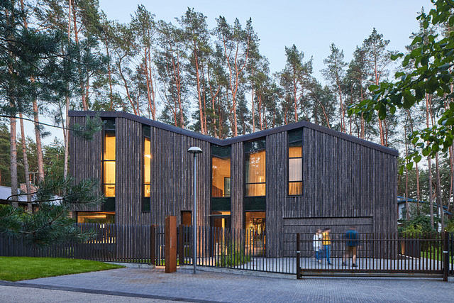 A modern, wooden cabin-like structure with large windows and a unique roofline amid trees.