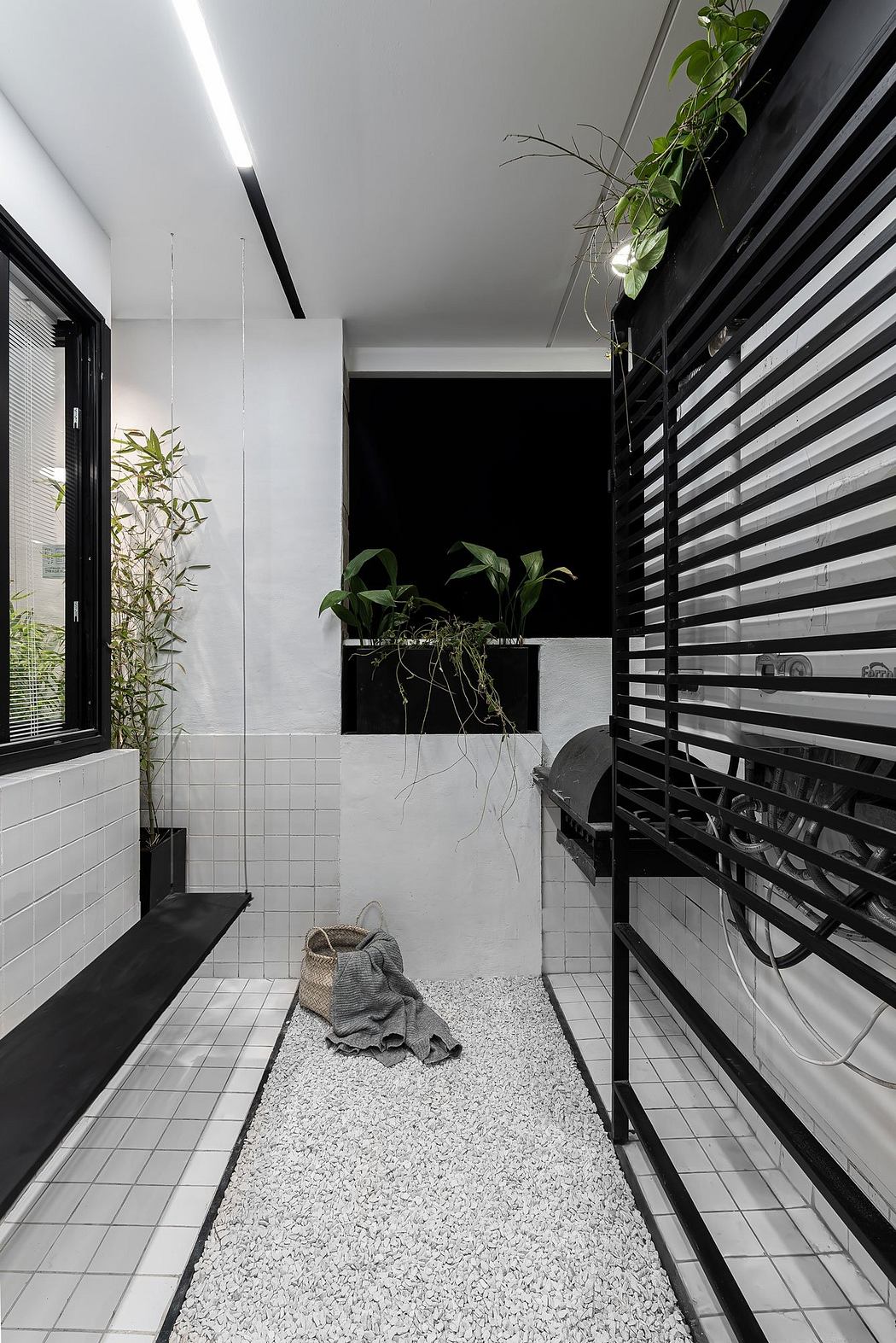 A modern, minimalist bathroom with black and white striped walls, a slate floor, and lush greenery.