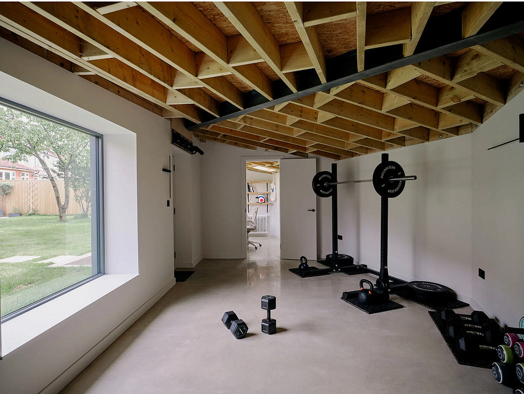 Spacious home gym with exposed wooden ceiling beams, large windows, and weightlifting equipment.