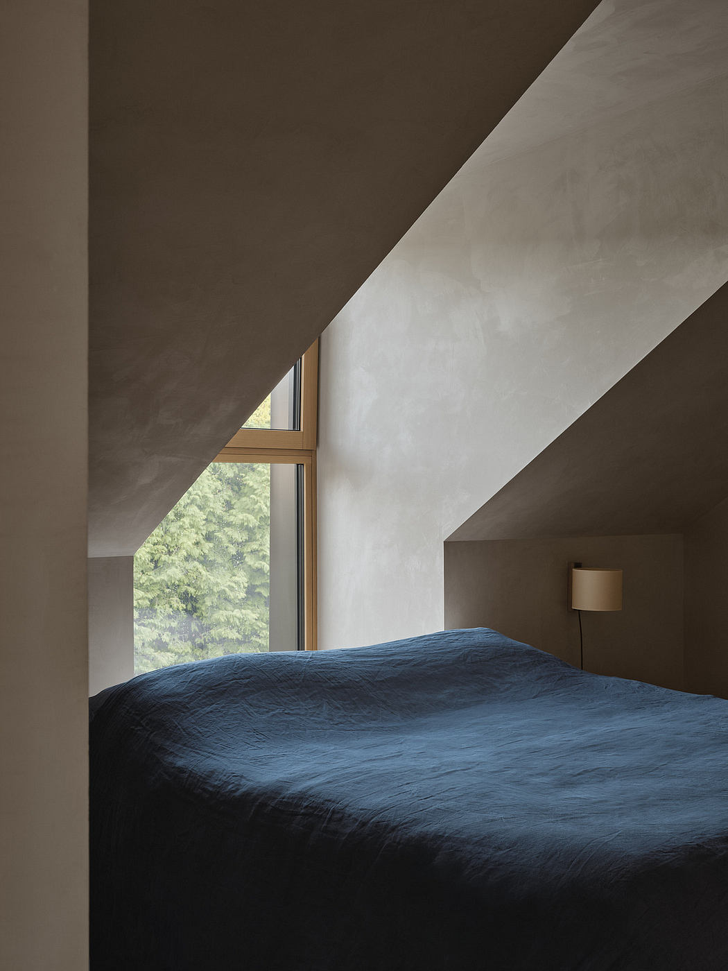 Minimalist bedroom design with large sloped windows overlooking lush greenery.