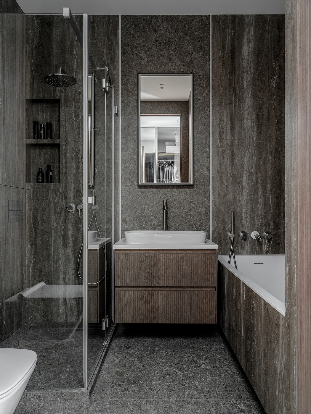 Sleek, modern bathroom with dark stone walls, glass shower, and minimalist vanity.