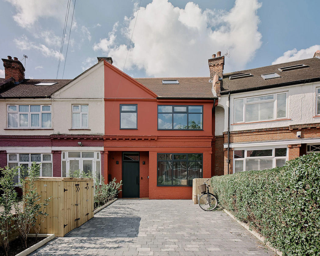 A charming, red-brick home with a distinctive triangular roof and paved entryway featuring a bicycle.