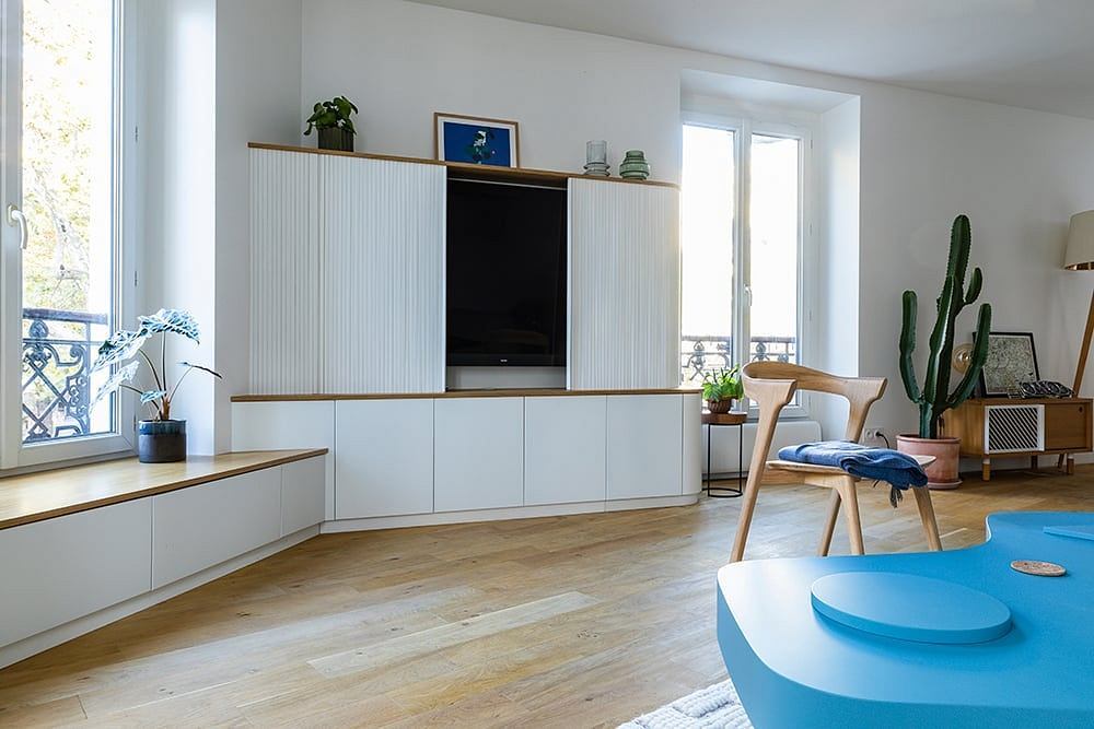 Bright, modern living room with built-in TV cabinet, wood floor, and potted plants.