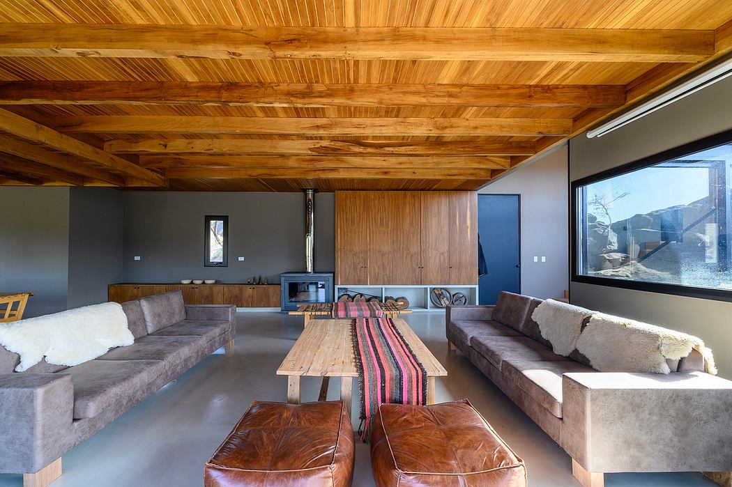 Rustic wooden beamed ceiling, grey sofas, leather ottomans, and natural light create a cozy space.