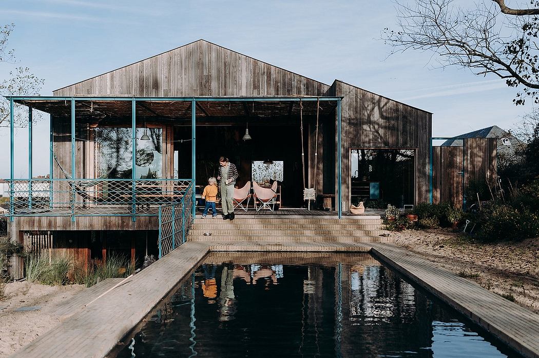 Rustic wooden cabin with open porch, pool, and reflection in water against blue sky.