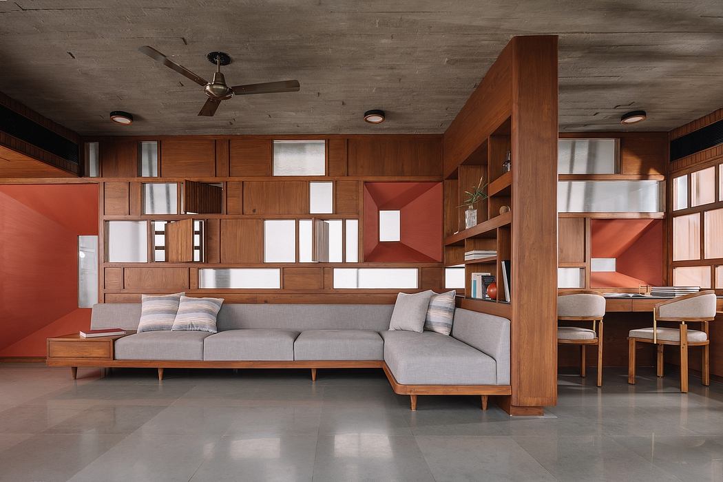 Warm-toned modern interior with wooden built-in shelving, modular gray sofa, and tile flooring.