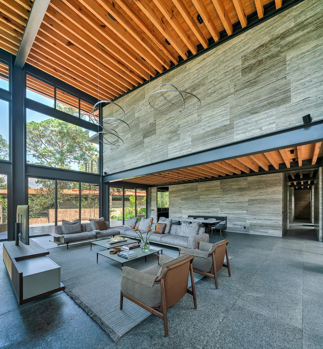 Expansive modern living space with a wood-paneled ceiling, stone-clad walls, and glass walls overlooking nature.