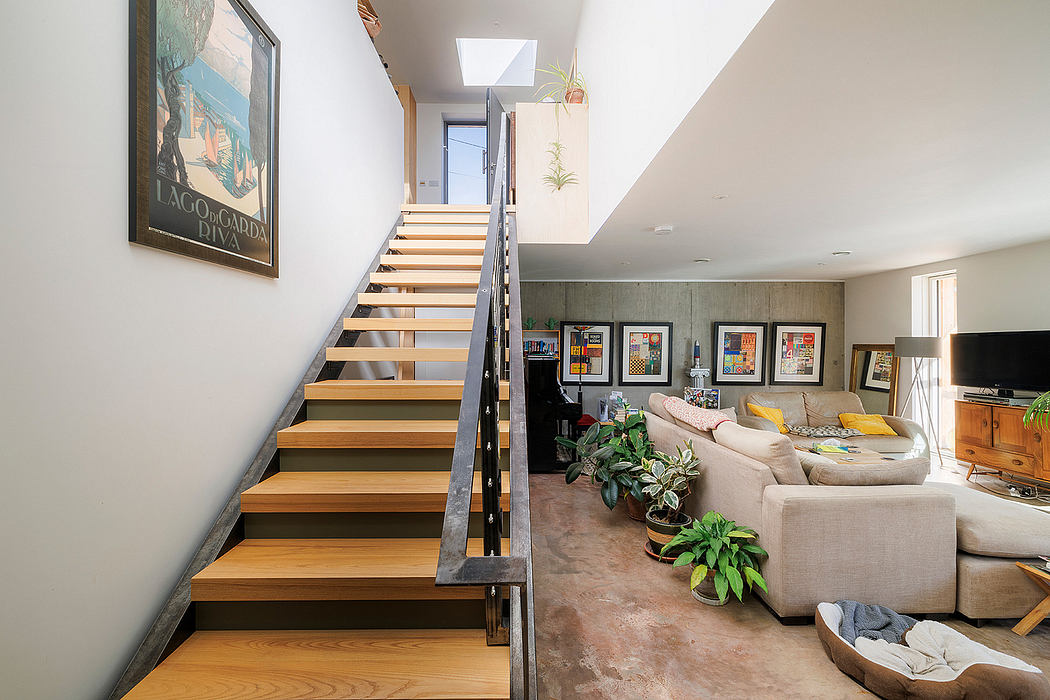 Bright, open-concept living space with wooden stairs, artwork, and potted plants.