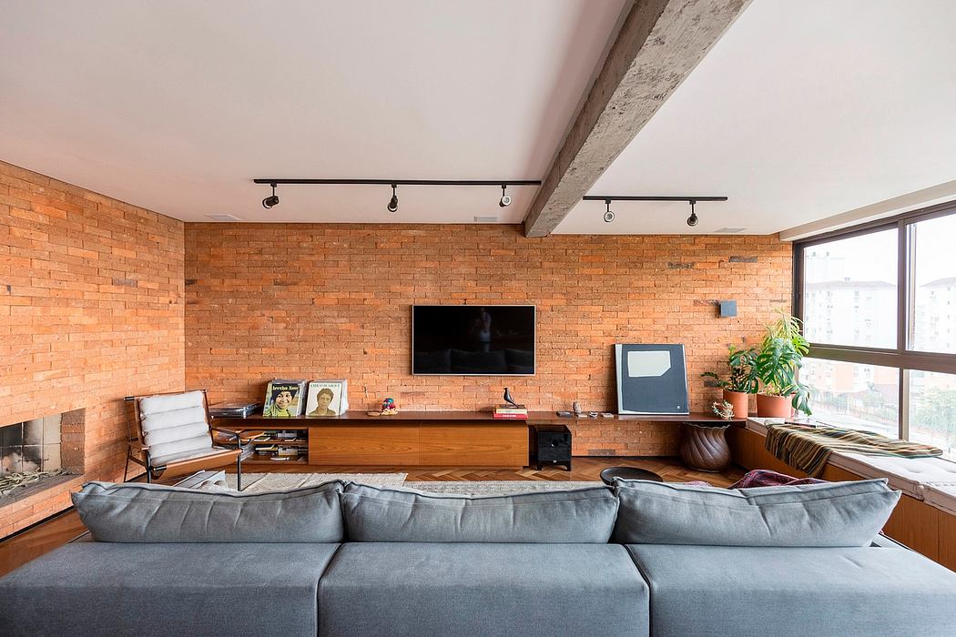 A cozy loft-style living room with exposed brick walls, track lighting, and a large gray couch.