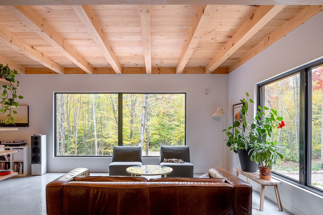 Spacious living room with wood-beamed ceiling, large windows overlooking scenic forest.