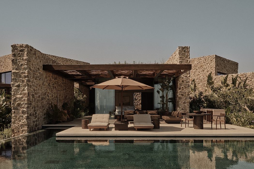 A stone villa with a covered patio, sun loungers, and a swimming pool reflecting the structure.