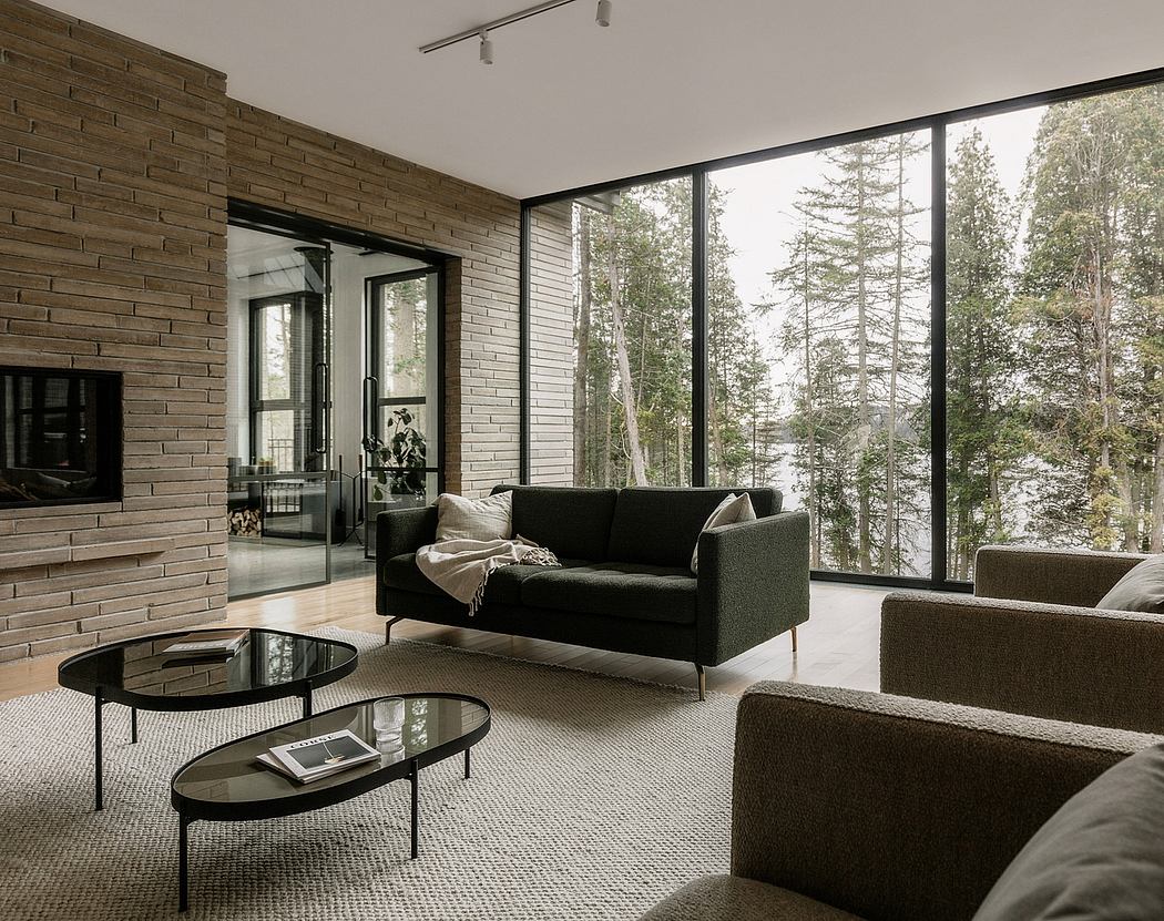Modern, minimalist living room with large windows overlooking forested landscape.