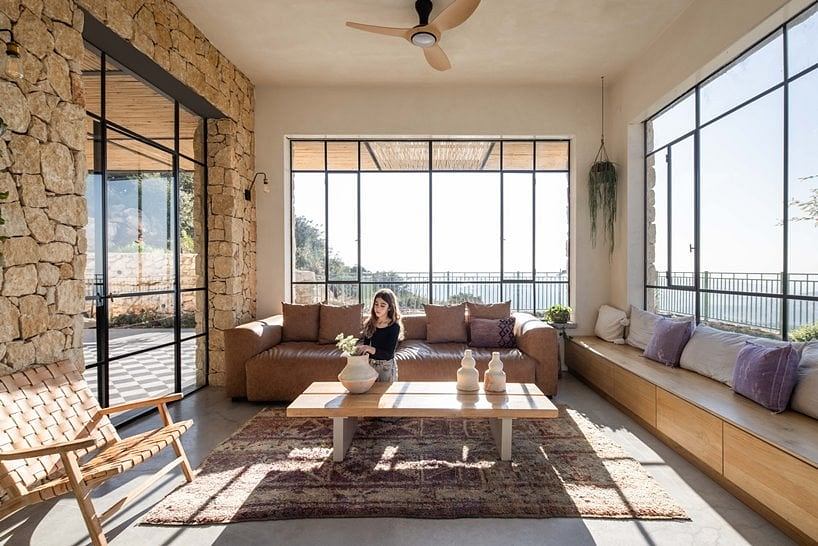 Warm, rustic living space with large windows, stone walls, and cozy seating arrangements.