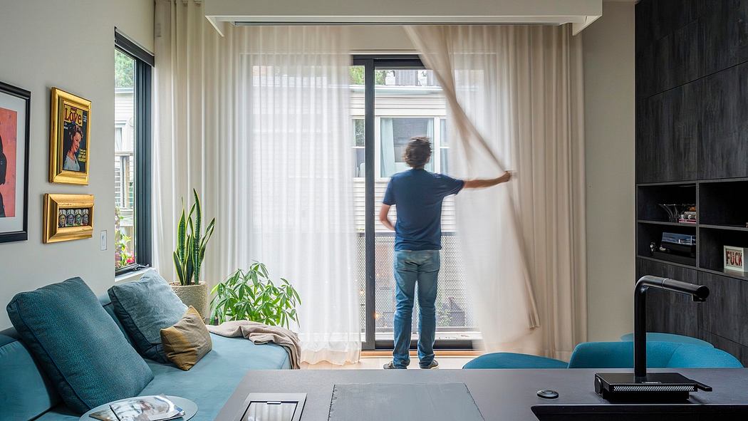 A cozy living room with modern furniture, large windows, and a person adjusting the curtains.