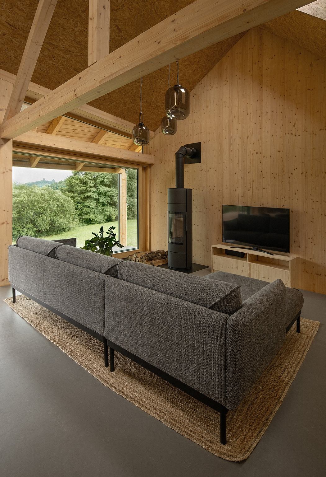 Cozy living room with wooden beams, hanging lights, and a modern, gray couch facing a TV.
