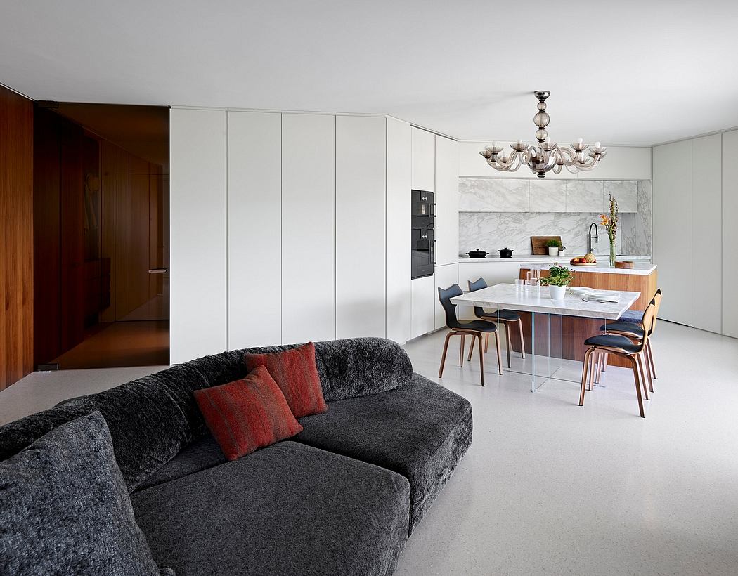 A modern, open-concept kitchen and living space with sleek cabinetry, marble countertops, and a chandelier.