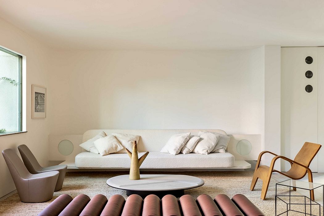 A minimalist living room with a large white sofa, a circular coffee table, and mid-century modern chairs.