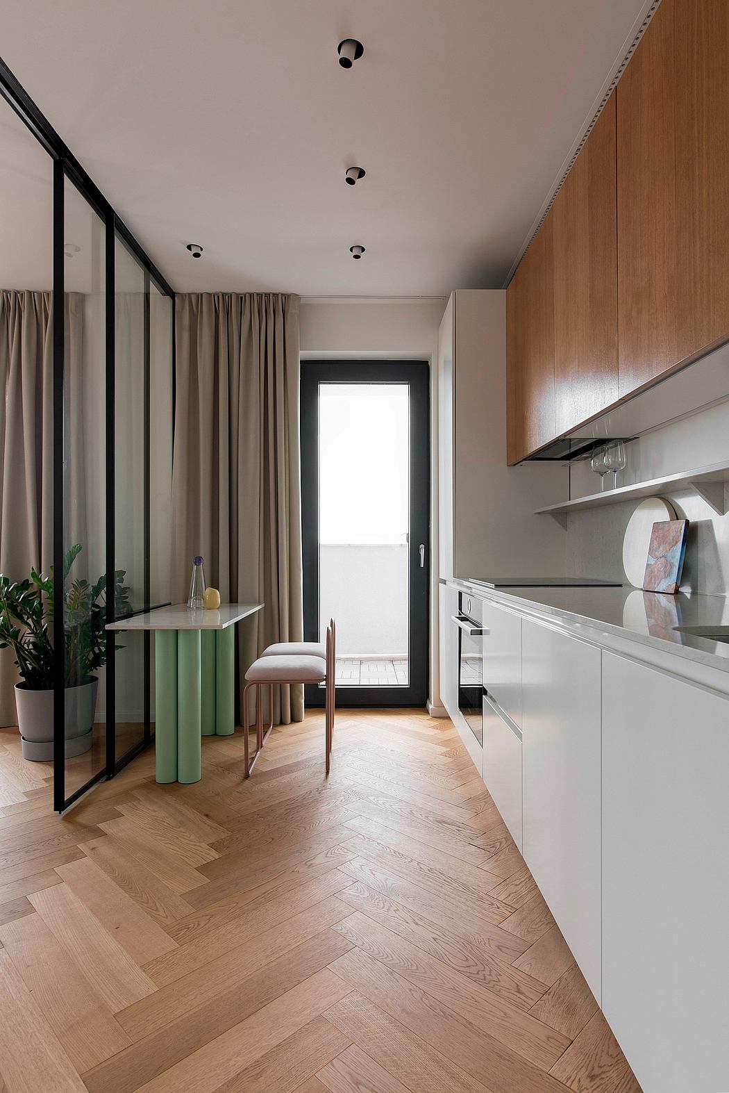 Minimalist kitchen space with wooden cabinets, curtains, and herringbone hardwood floors.