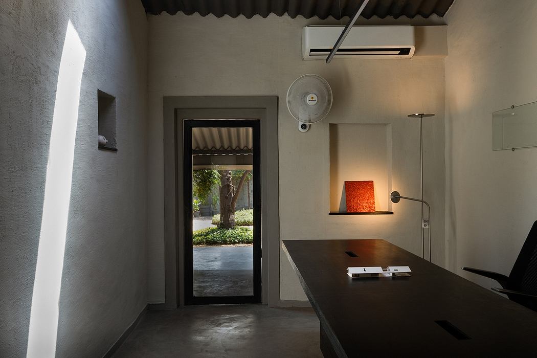 A modern, minimalist workspace with a view of a garden through a glass door and shelving unit.