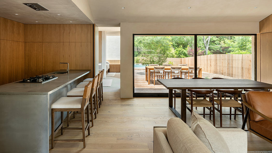 Modern, open-plan kitchen and dining area with wooden cabinetry, large windows, and an outdoor patio.