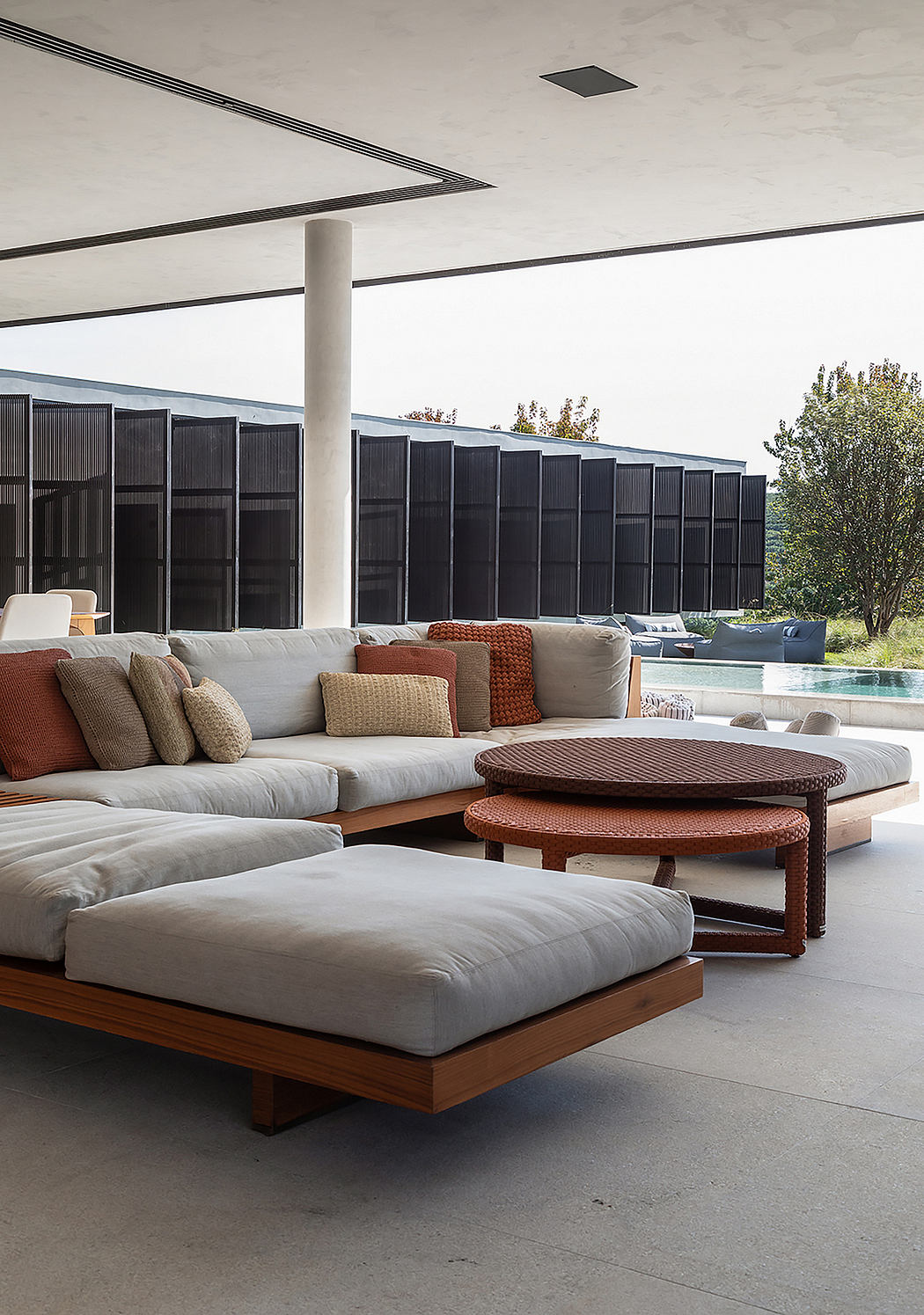 A modern, minimalist outdoor seating area with low-profile sofas, round tables, and a sleek architectural backdrop.