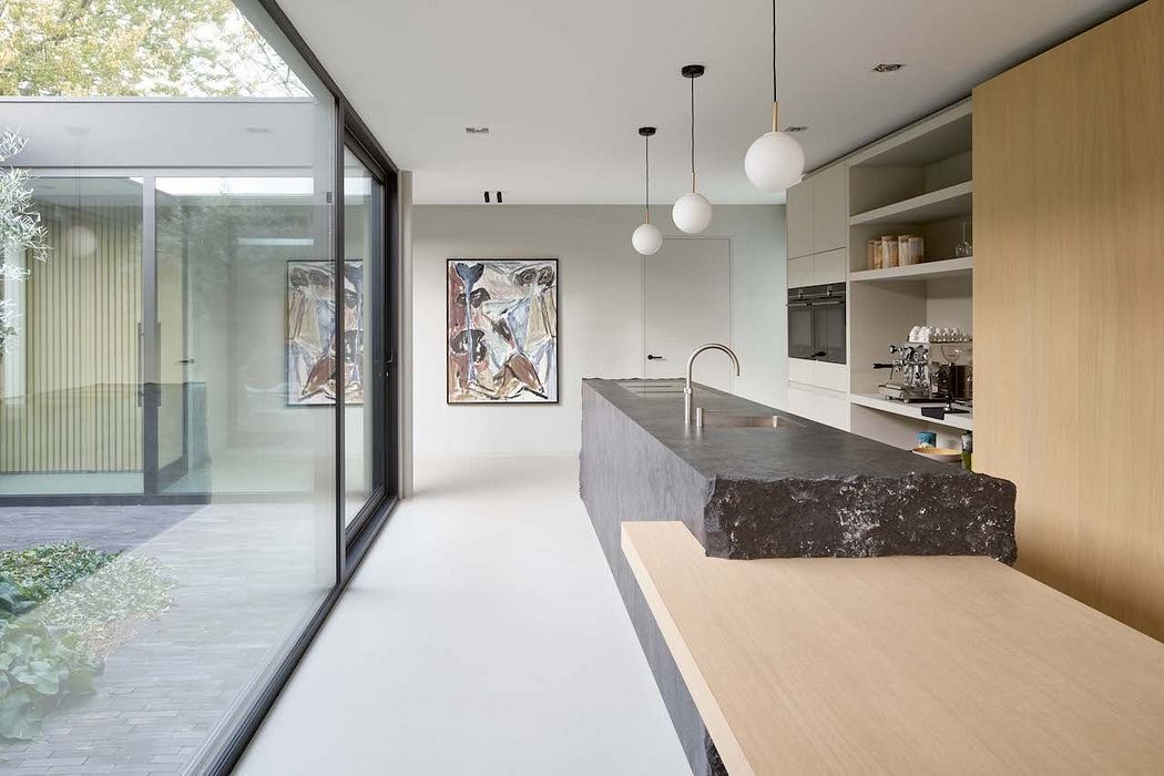 Minimalist kitchen with concrete island, artwork, and large glass windows overlooking nature.