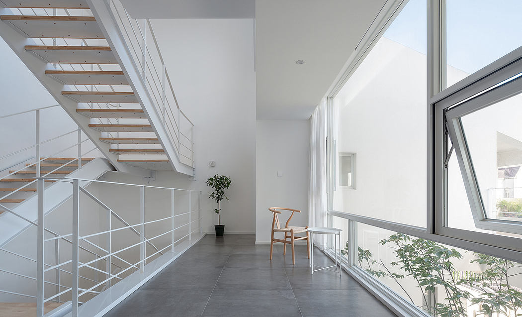 A modern, minimalist interior with an open staircase, large windows, and potted plants.