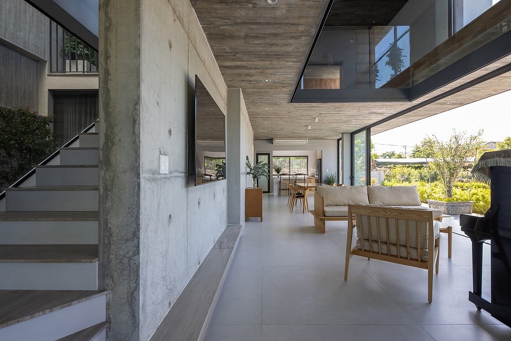 Modern open-plan interior with concrete walls, wooden beams, and large windows overlooking greenery.