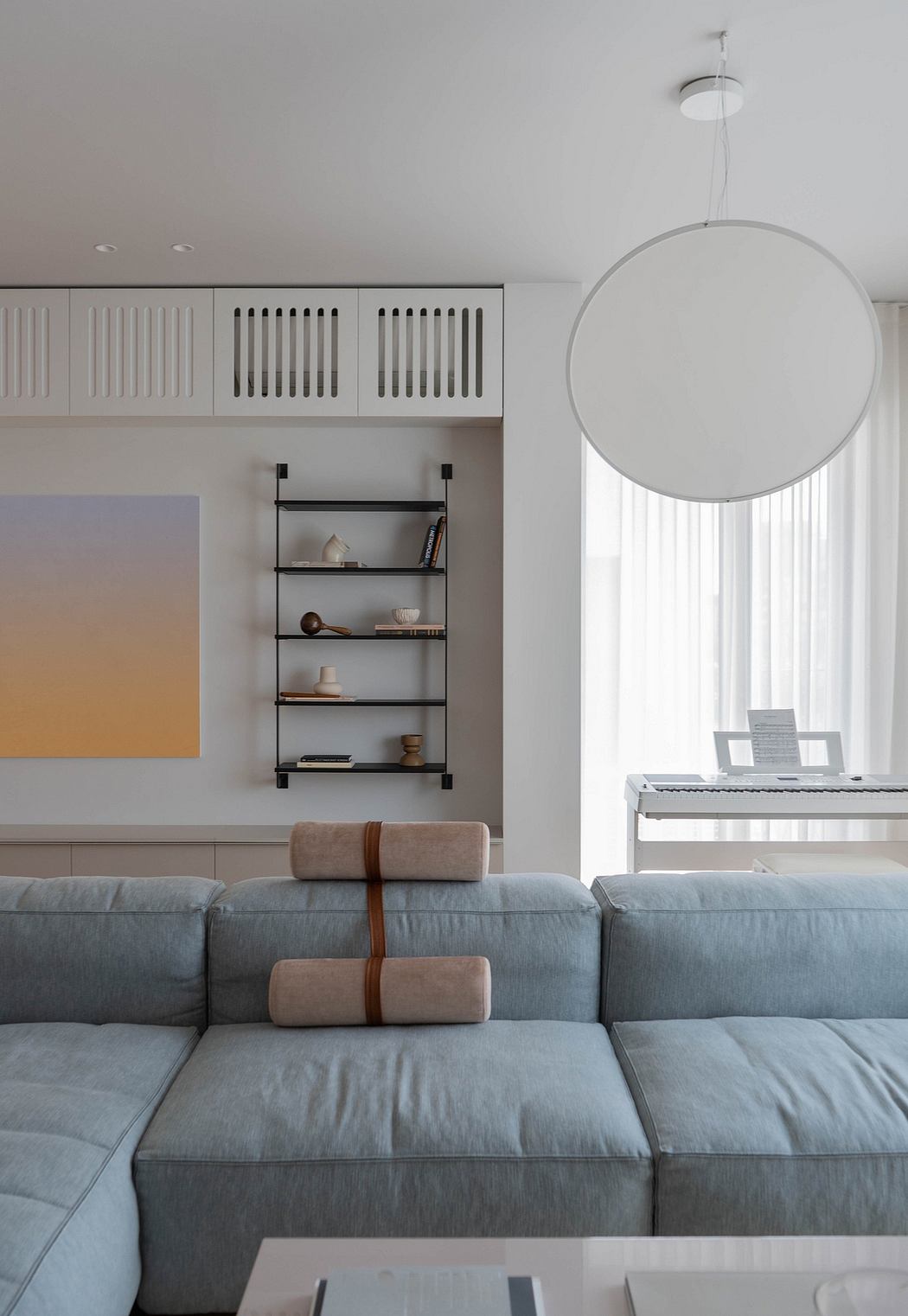 A modern living room with a comfortable gray sectional sofa, built-in shelving, and a large round pendant light.
