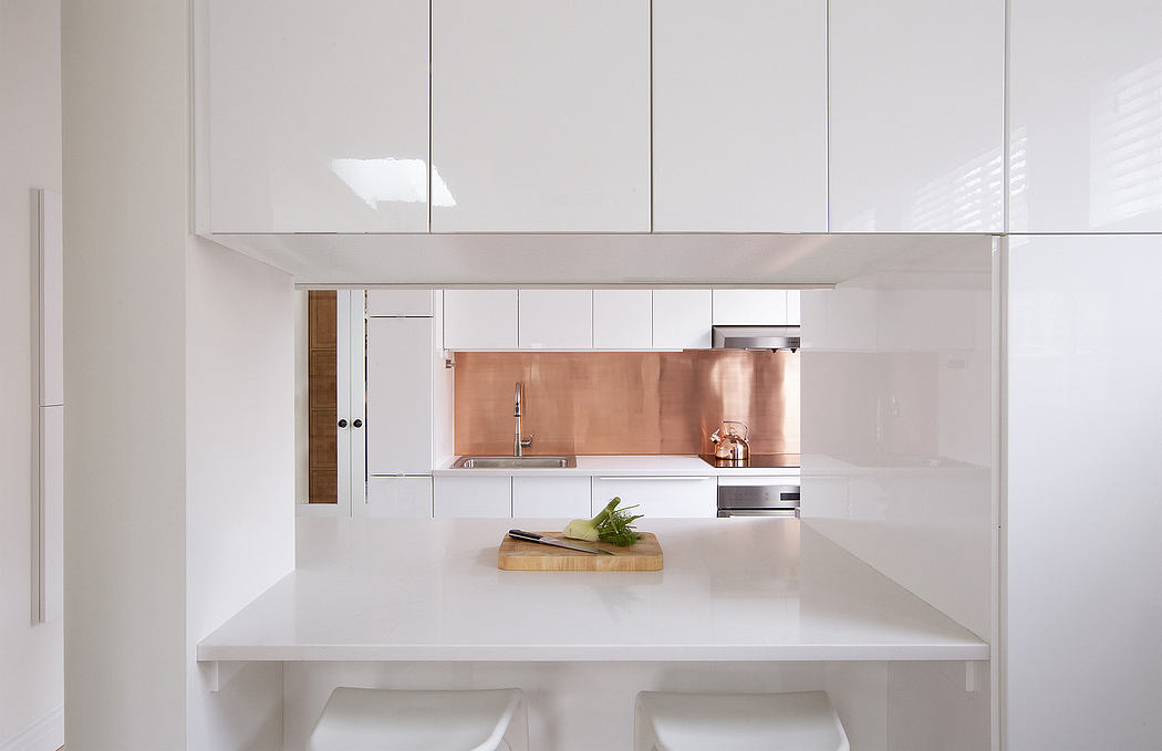Minimalist kitchen design with sleek white cabinets, copper backsplash, and wooden details.