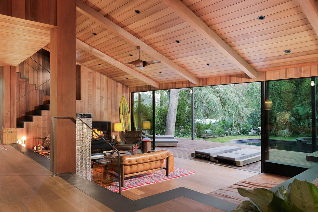 Open and spacious living room with vaulted wood-paneled ceiling, fireplace, and glass walls overlooking lush outdoor scenery.